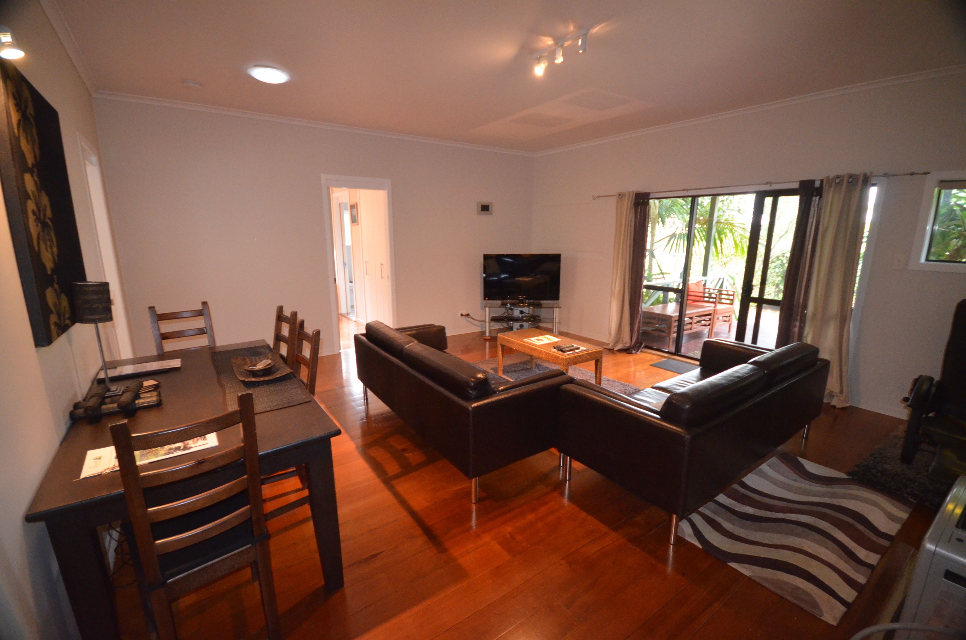 A living room with a wooden dining table, leather sofa, and a flat-screen TV.