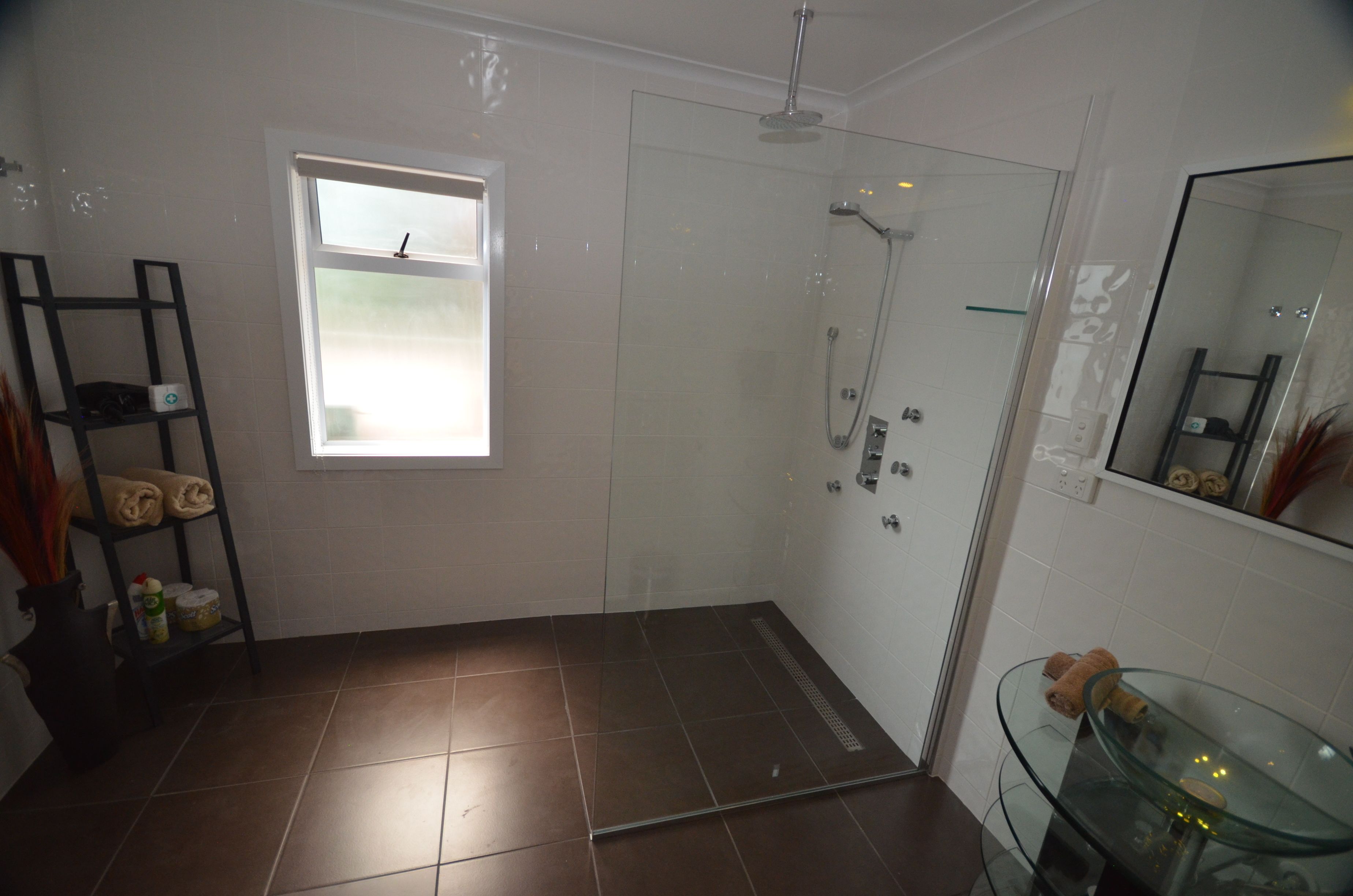 Un baño con cabina de ducha de vidrio, lavabo de vidrio y estante con toallas.