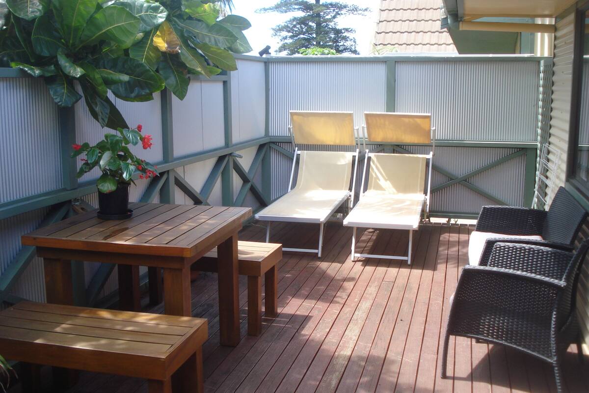 Un patio al aire libre con muebles de madera, incluyendo una mesa y sillas, y una planta en maceta.