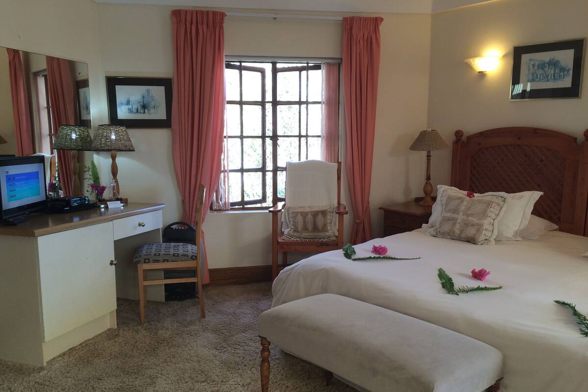 A hotel room with a bed, a desk with a computer, a chair, a window with curtains, and a bedside lamp.