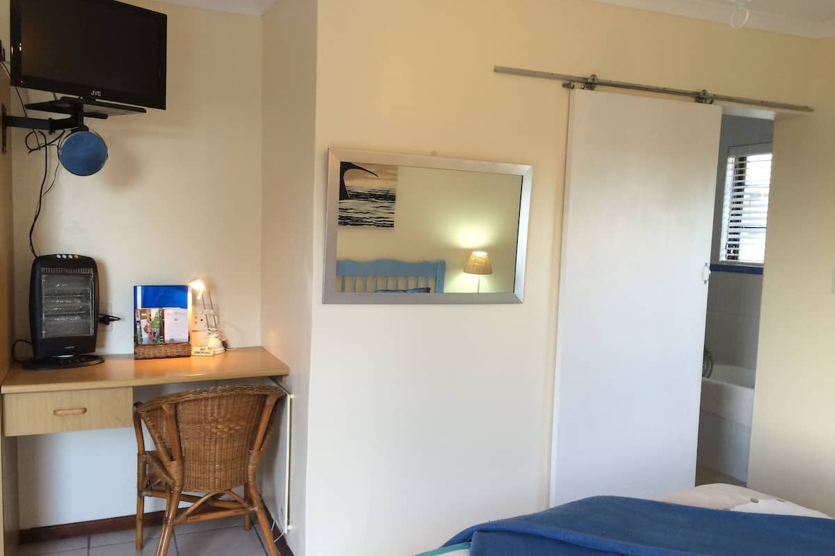 A hotel room with a bed, a desk with a computer, a chair, a television, and a mirror.