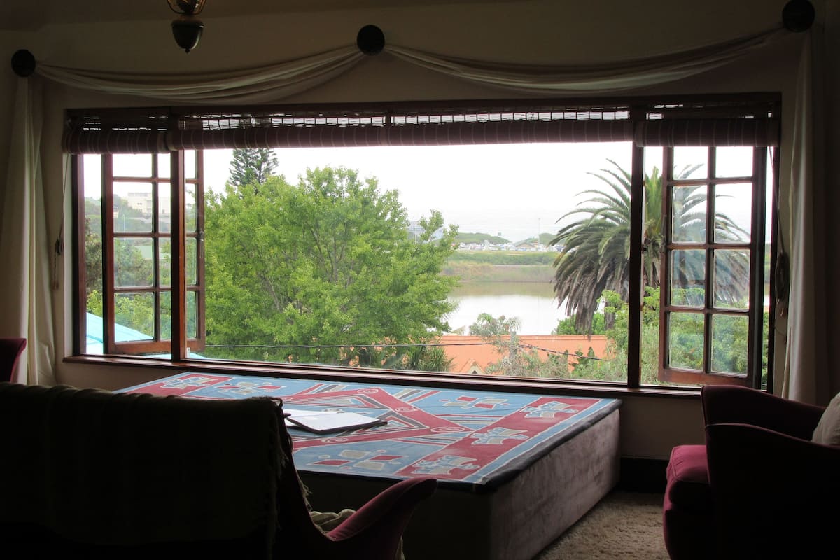 A room with a large window, a table with a patterned tablecloth, and two chairs.