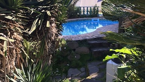 A pool area with a stone pathway leading to a pool surrounded by lush greenery and palm trees. - Mont Fleur B&B (Wilderness)