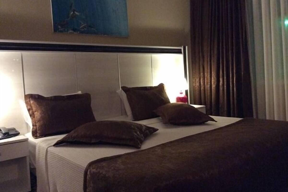 A hotel room with a large bed, two pillows, a nightstand with a phone, and a painting on the wall.