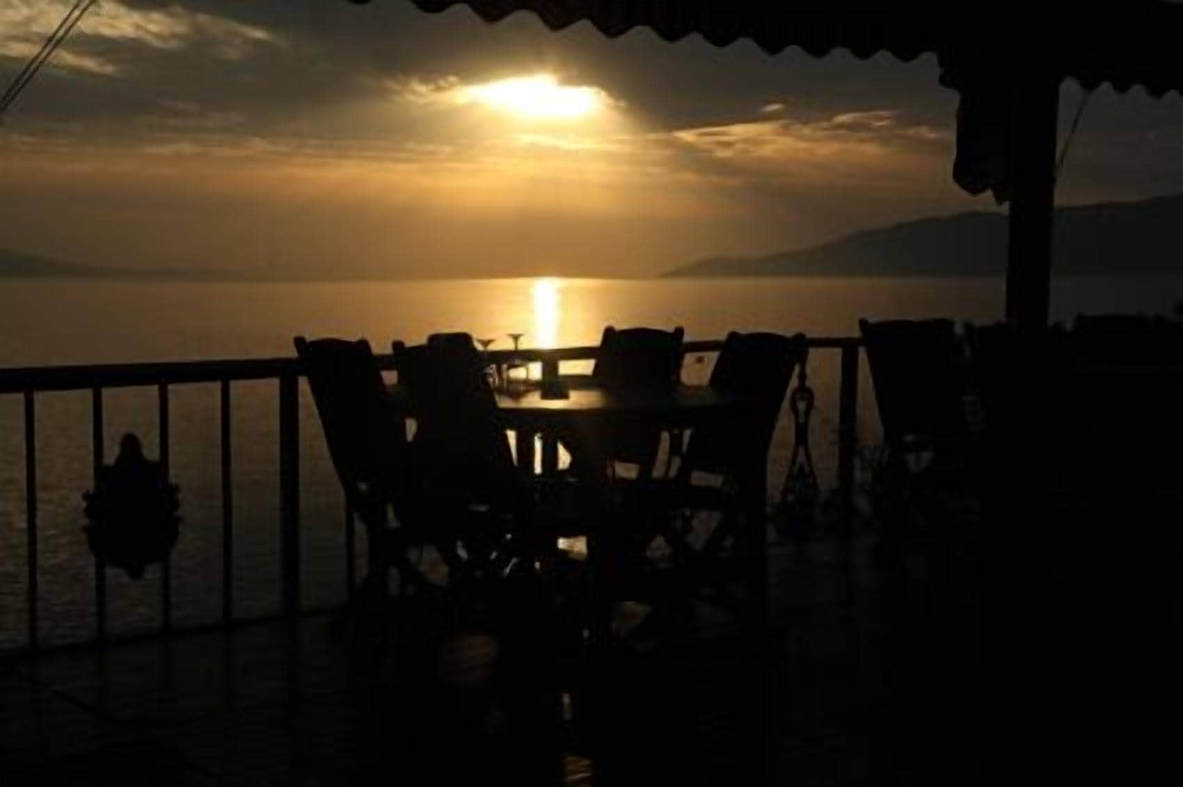 Une table et des chaises sur un balcon, avec vue sur le coucher de soleil sur l’eau.