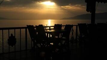 Une table et des chaises sur un balcon, avec vue sur le coucher de soleil sur l’eau.