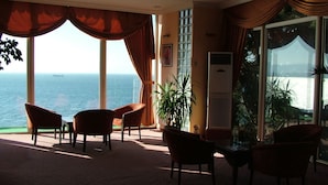 A room with a view of the sea, featuring a sofa, chairs, a table, and a potted plant. - Atamer Hotel (Gemlik)
