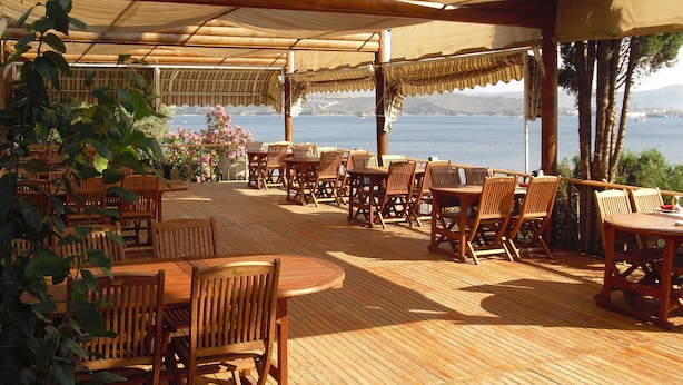 A wooden deck with tables and chairs, overlooking a body of water. - Atamer Hotel (Gemlik)