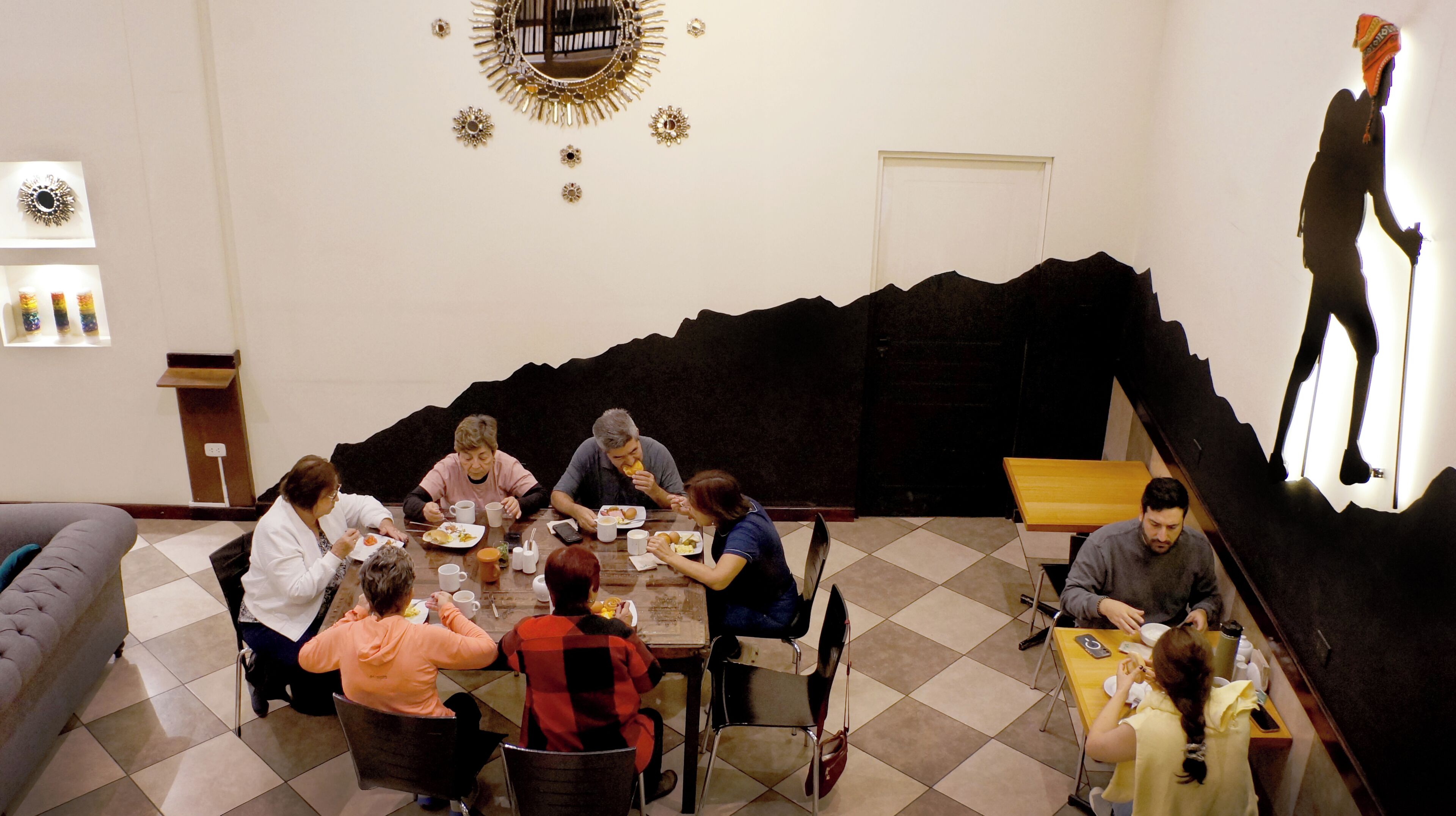 Un comedor con un grupo de personas sentadas alrededor de una mesa, un elemento decorativo en una pared negra y un ventanal con vistas.