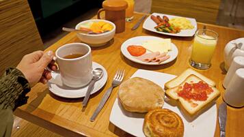 Una mesa de desayuno con una taza de café, un plato de huevos, salchichas, tostadas con mermelada, un muffin y un bol de fruta.