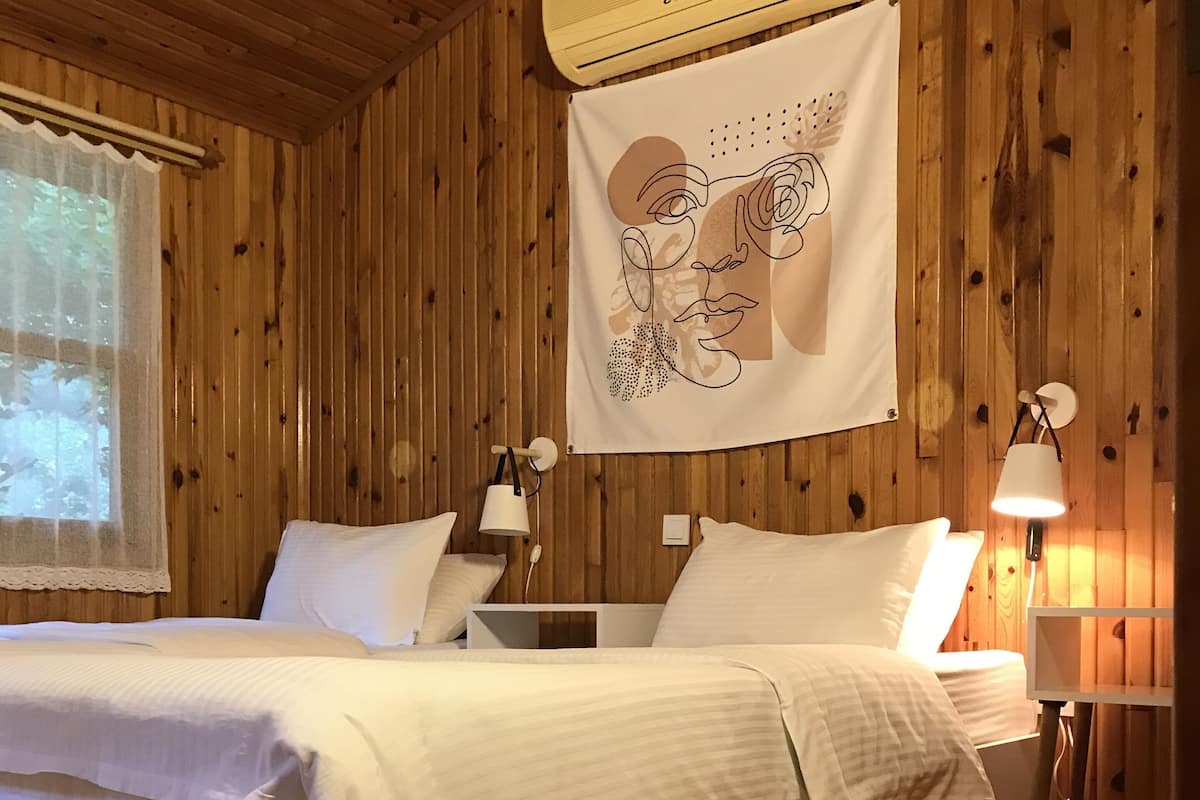 Een kamer met houten lambrisering, een bed, twee bedlampen, een airconditioner en een wanddecoratie.