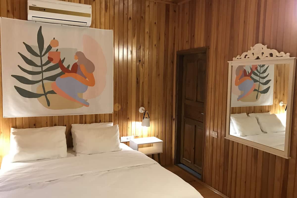 Een kamer met houten lambrisering, een bed, een wandairconditioner, een spiegel en een schilderij.