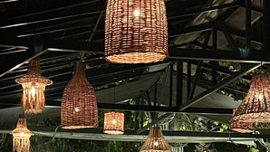 Un restaurant avec des lampes suspendues en osier, un coin bar et de la verdure en arrière-plan.