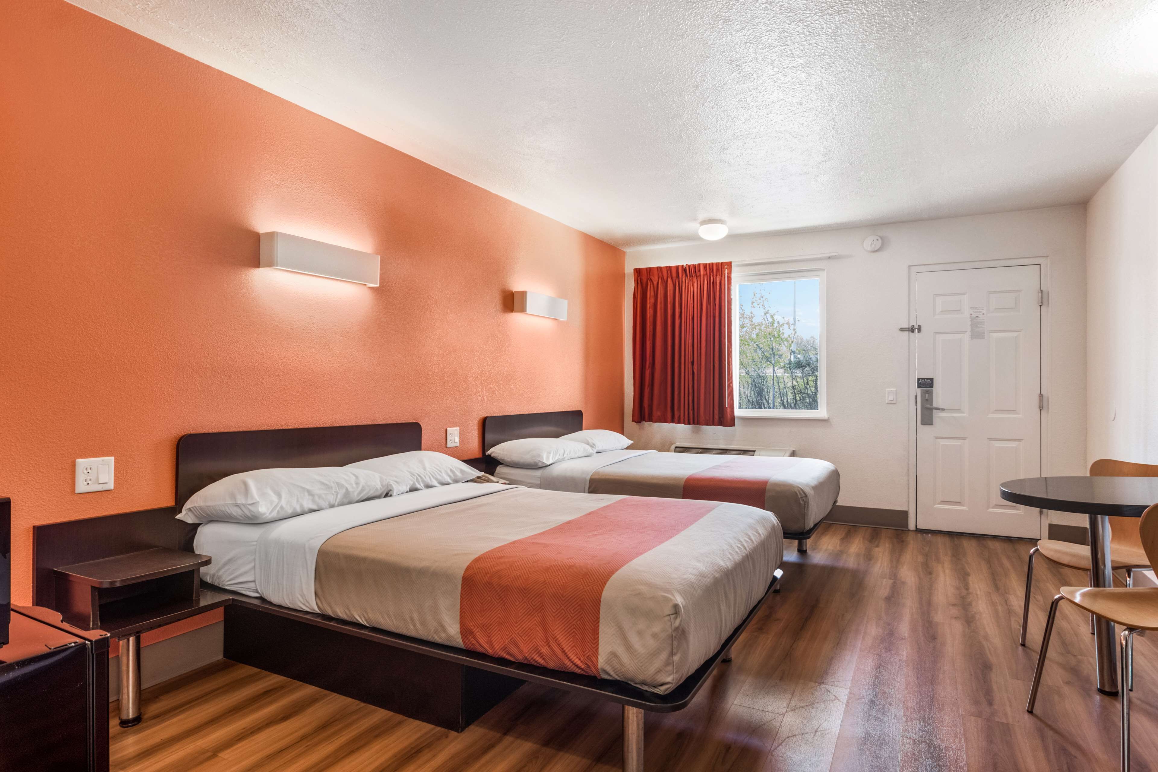 A hotel room with two beds, a desk, a chair, and a window with curtains.