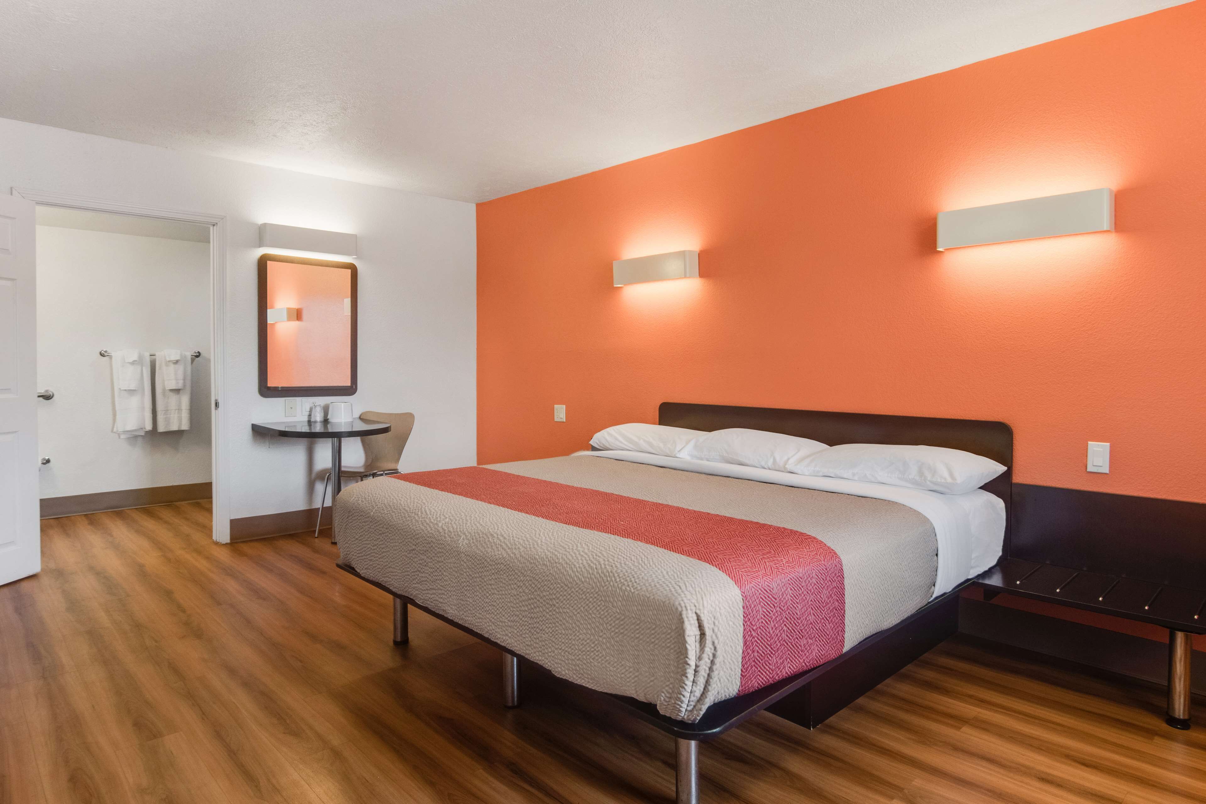 A hotel room with a bed, a small table, a chair, a mirror, and a bathroom door.