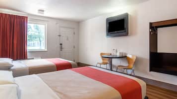 A hotel room with two beds, a TV, a small table with chairs, and a window with curtains.