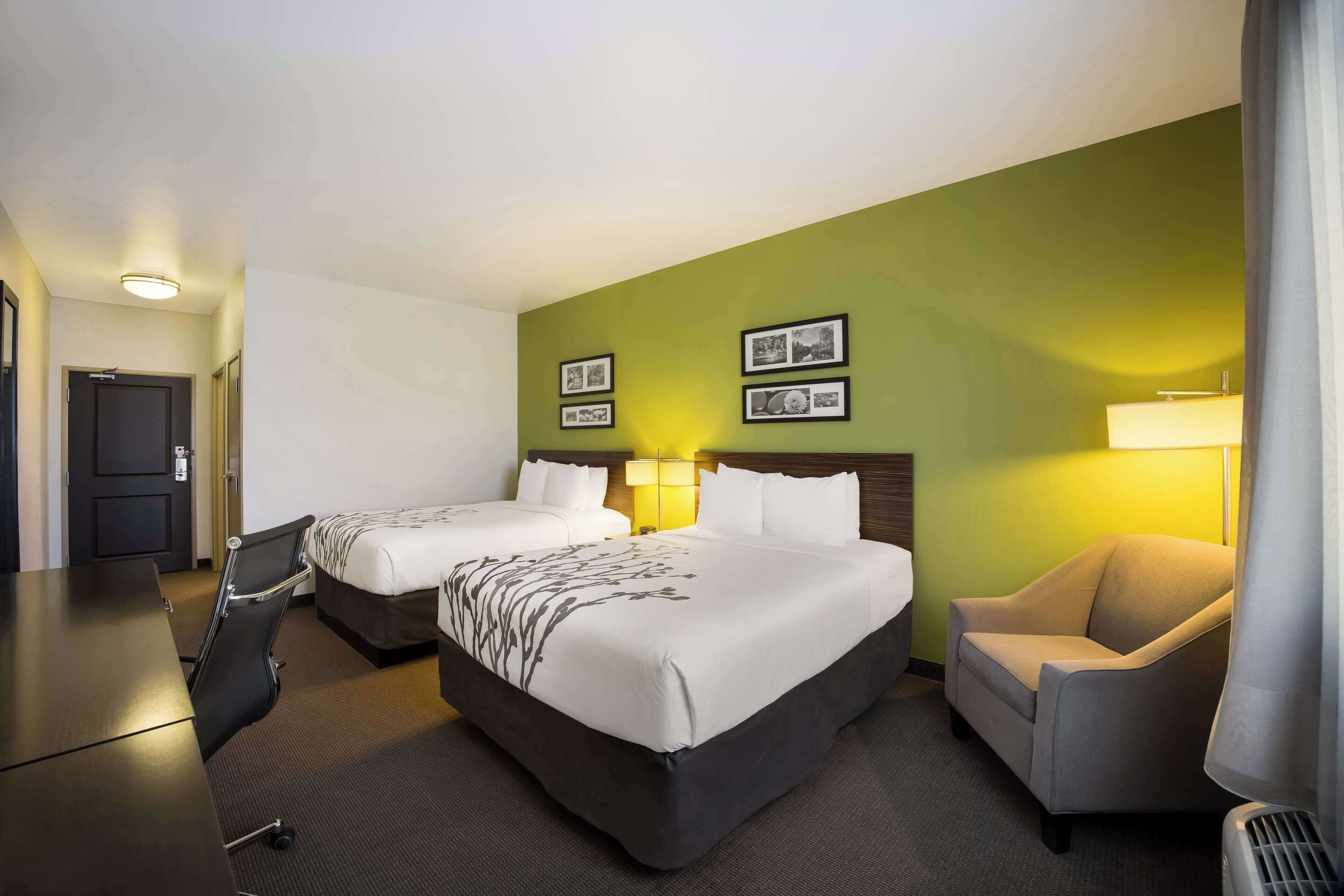 A hotel room with two beds, a desk, a chair, and a lamp.