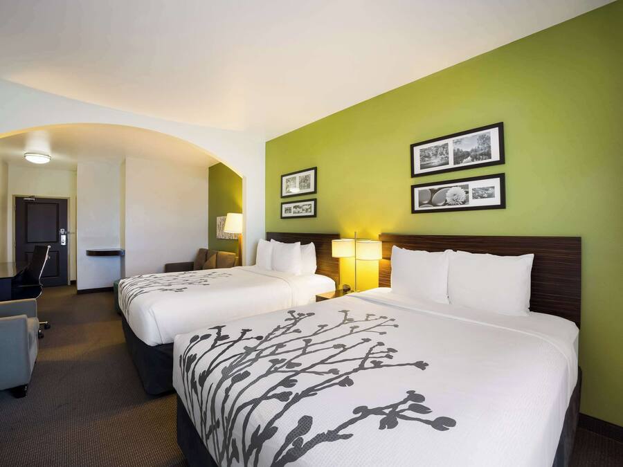Ett hotellrum med två sängar, ett skrivbord och en stol. Det finns inramade tavlor på väggen.