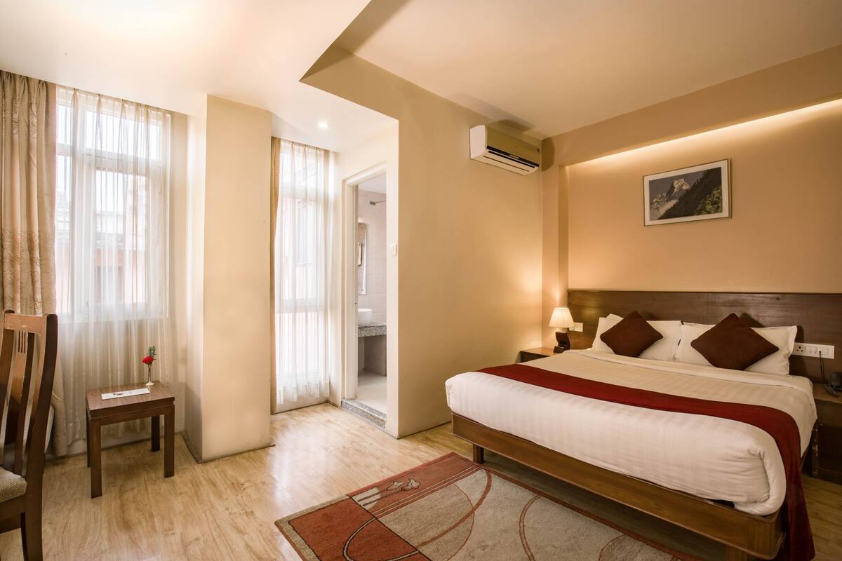 A hotel room with a bed, bedside table, lamp, and a view of the bathroom.