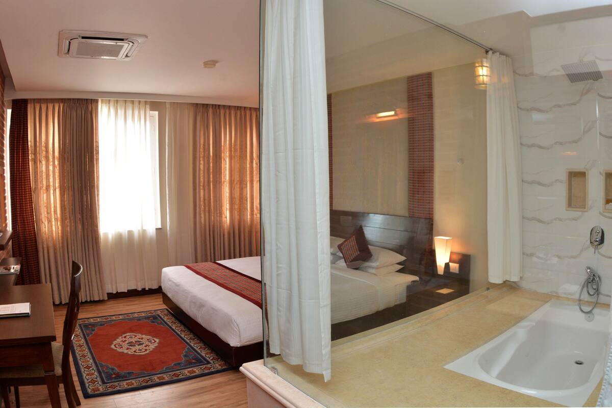 A hotel room with a bed, a desk, a chair, a bathroom with a bathtub, and a shower.