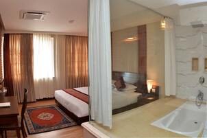 A hotel room with a bed, a desk, a chair, a bathroom with a bathtub, and a shower.