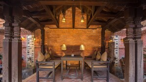 A covered outdoor seating area with a brick wall background, wooden pillars, and hanging lights. - Hotel Marshyangdi (Kathmandu)