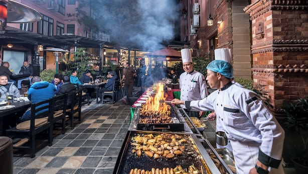 An outdoor dining area with a grill station and seated guests. - Hotel Marshyangdi (Kathmandu)