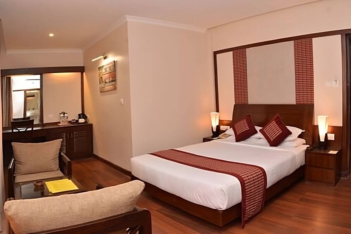 A hotel room with a large bed, a desk, a chair, and a mirror.