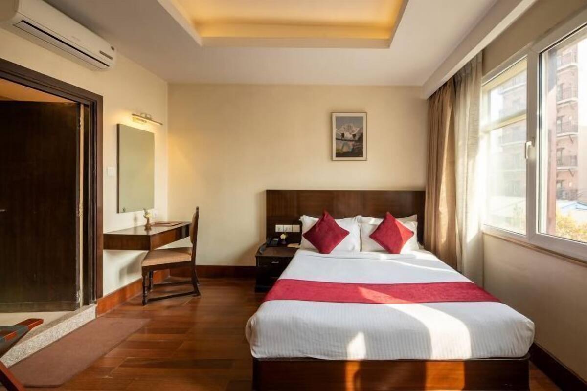 A hotel room with a bed, a desk, a chair, a nightstand, a mirror, and a window.