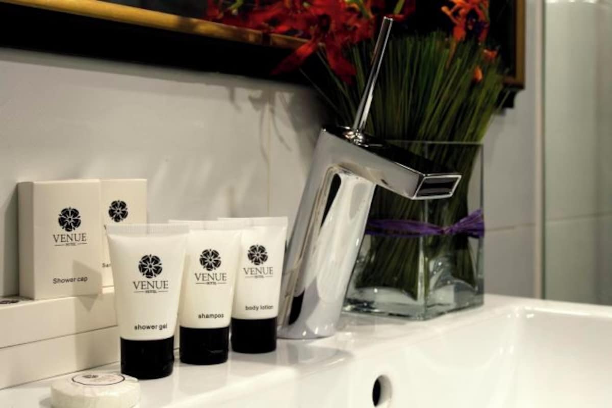 A bathroom with a white sink, a shower cap, and three VENUE toiletries (shower gel, shampoo, body lotion).