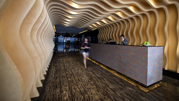 A hotel lobby with a wavy ceiling design, a reception desk, and a patterned floor. - Venue Hotel (Singapore)