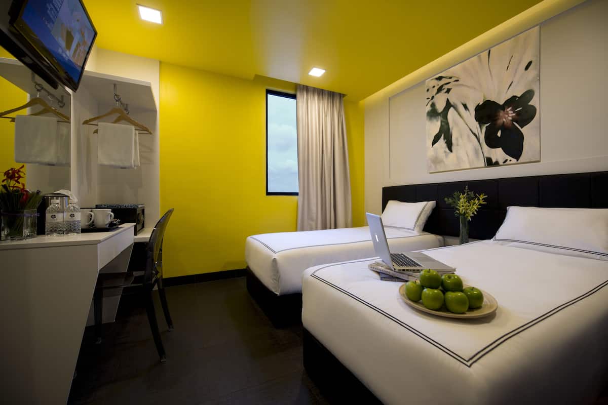 Habitación de hotel con dos camas, un escritorio con una computadora portátil, un televisor y un cuadro en la pared.