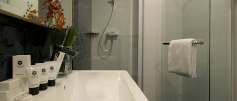 Un baño moderno con un lavamanos blanco, cabina de ducha de vidrio y un perchero para toallas.