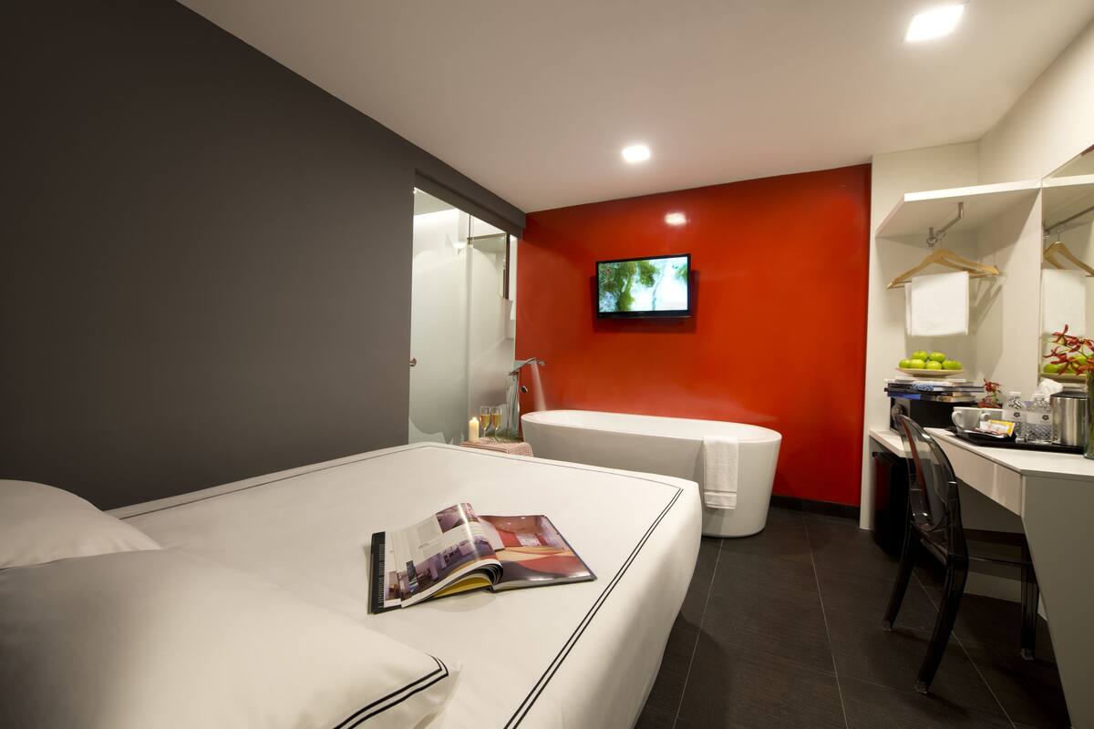 Una habitación de hotel moderna con cama, escritorio, silla, televisión y baño.