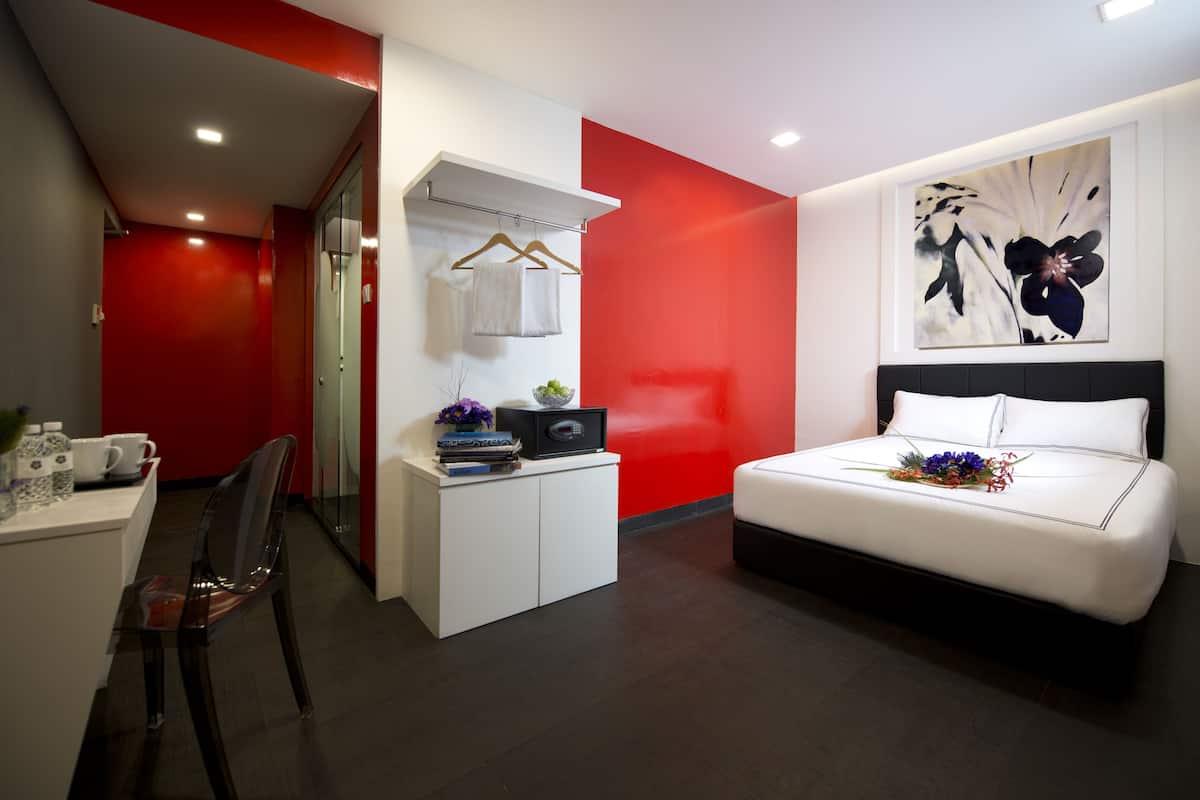 Una habitación de hotel moderna con una cama blanca, paredes de acento rojas, un escritorio con silla y una pequeña zona de estar.