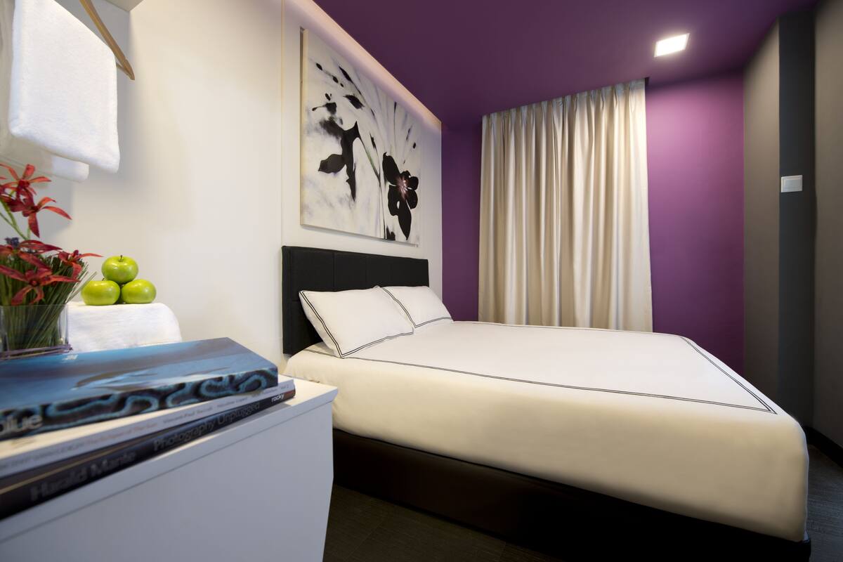 Un dormitorio moderno con una cama, una mesita de noche, una obra de arte en la pared y un ventanal con cortinas.