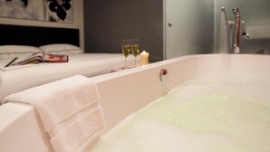 A bathroom with a bathtub, a towel, and two glasses of champagne on the edge. - Venue Hotel (Singapore)