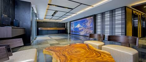A modern lobby with a large wooden coffee table, seating area, and a large digital screen displaying a scenic image.
