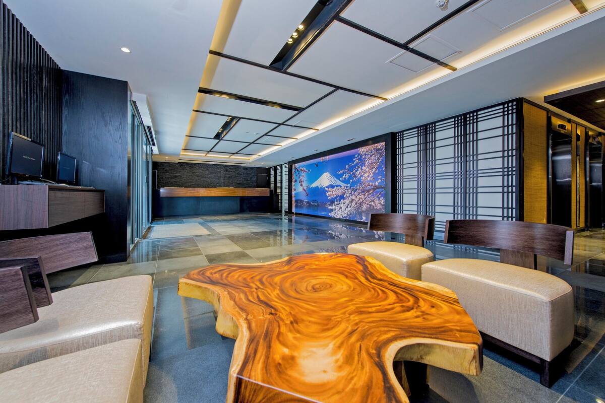 A modern lobby with a large wooden coffee table, seating area, and a large screen displaying a scenic image.