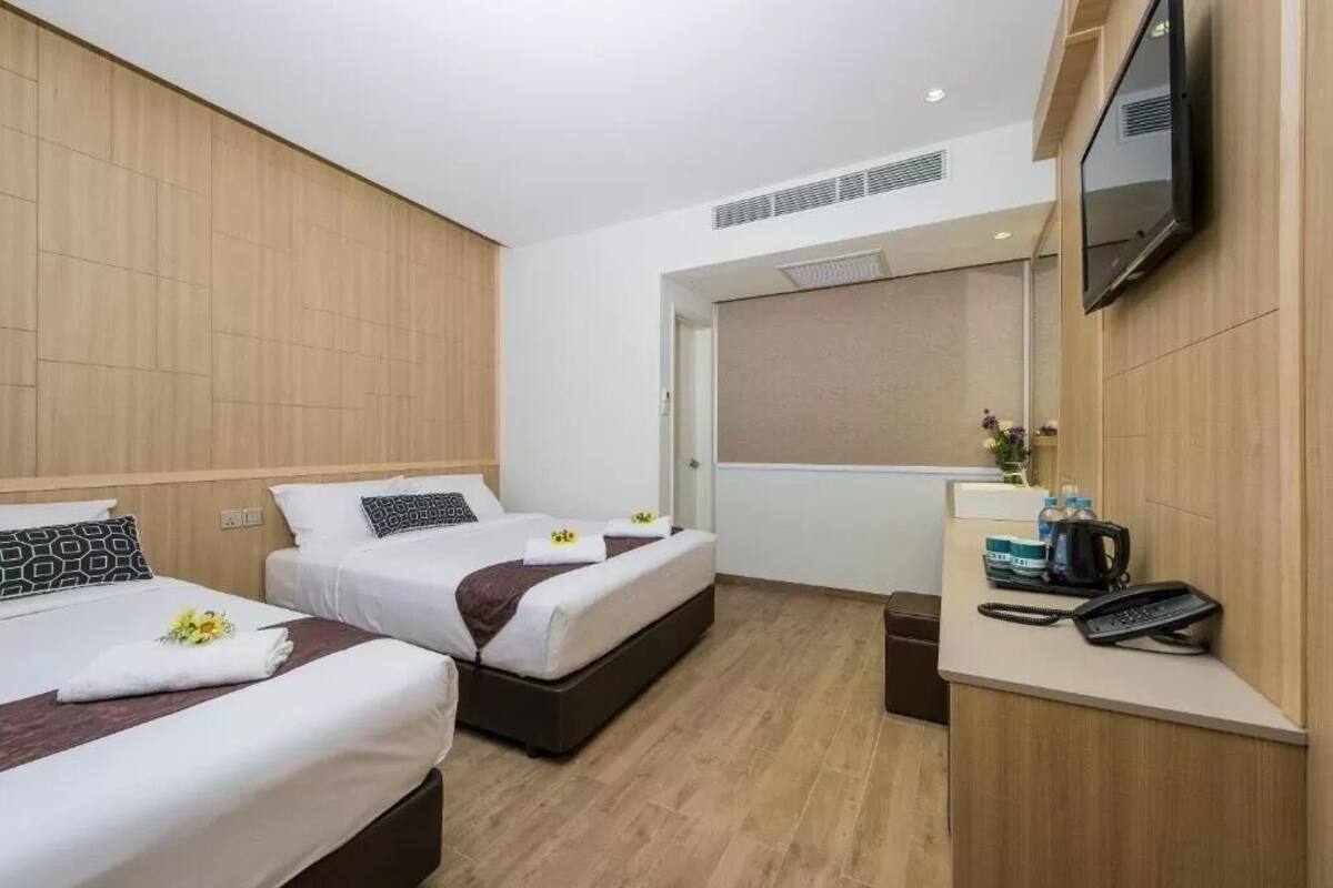 A hotel room with two beds, a desk with a telephone, and a television mounted on the wall.
