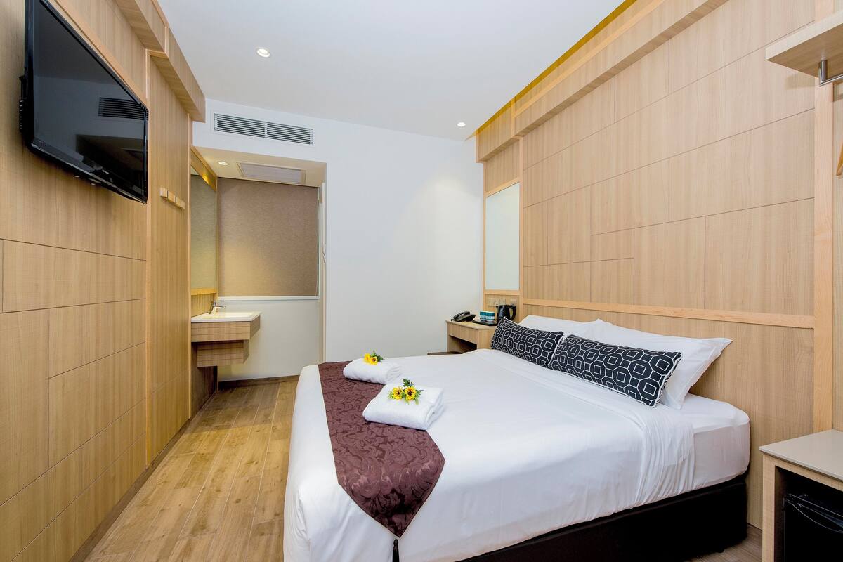 A hotel room with a bed, a TV mounted on the wall, a bedside table, and a mirror.
