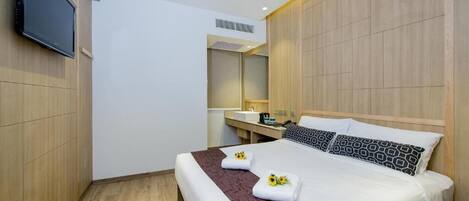 A hotel room with a large bed, a TV mounted on the wall, a wooden panel wall, and a small bathroom area.