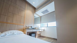 A modern hotel room with a wooden headboard, a bed with white linens, a small desk with a chair, and a window providing natural light. - Hotel 81 Premier Star (Singapore)