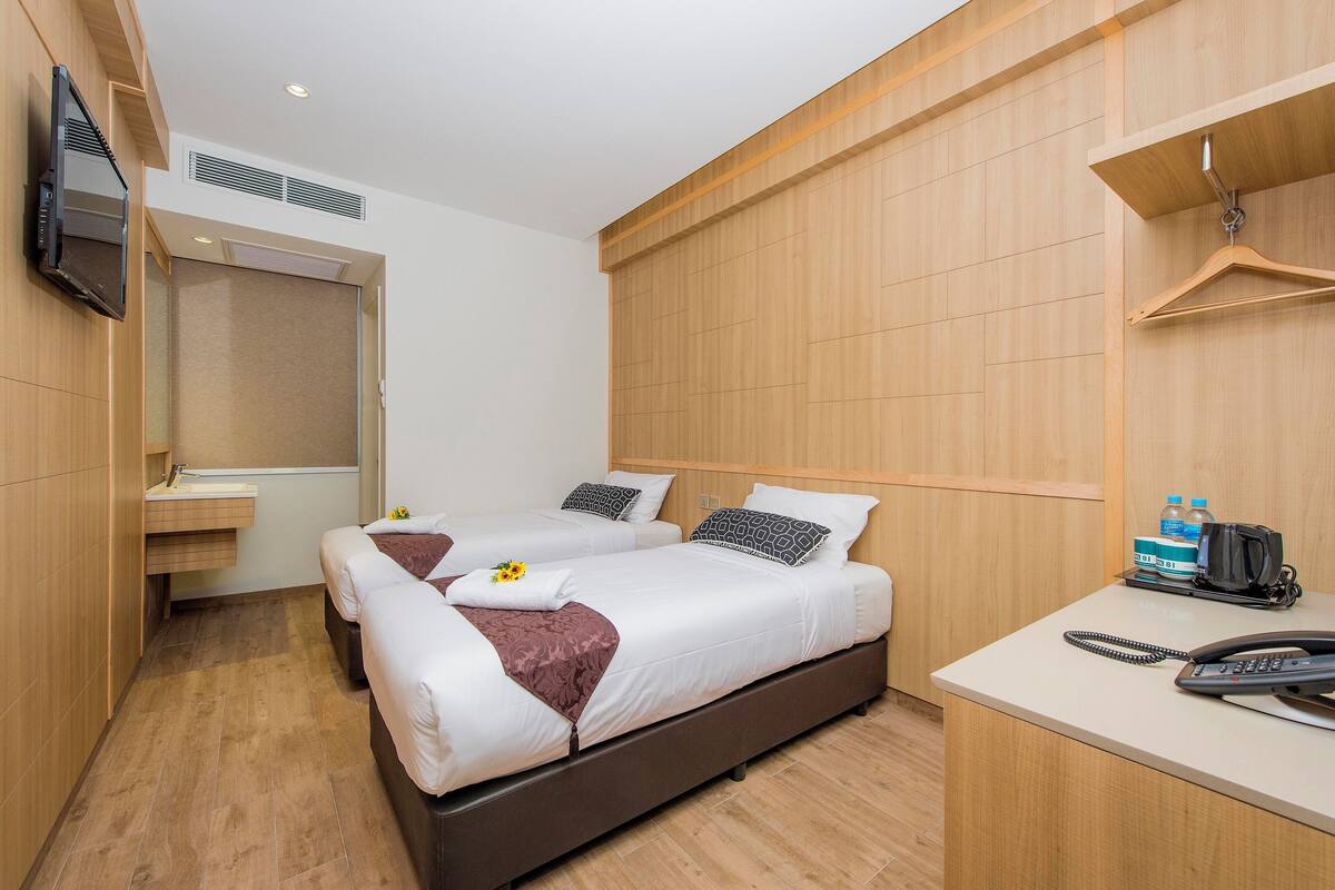 A hotel room with two beds, a desk with a telephone, and a television mounted on the wall.