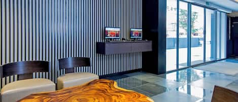 Un vestíbulo moderno con una mesa de madera, asientos, un televisor y un mostrador de recepción.
