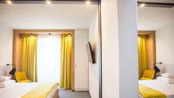 Quarto de hotel com duas camas, cortinas amarelas, televisão de tela plana e porta de madeira.