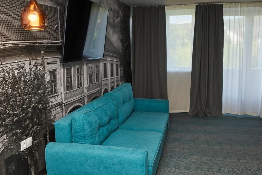 A room with a teal sofa, a wall-mounted TV, and a large window with curtains.