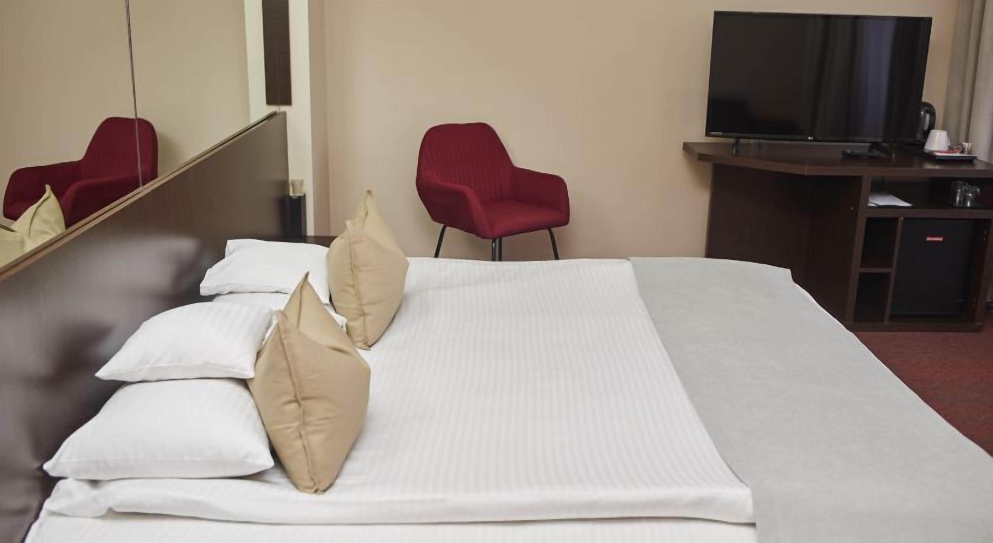 Une chambre d’hôtel avec un grand lit, deux fauteuils rouges, une télévision et un mini-bar.