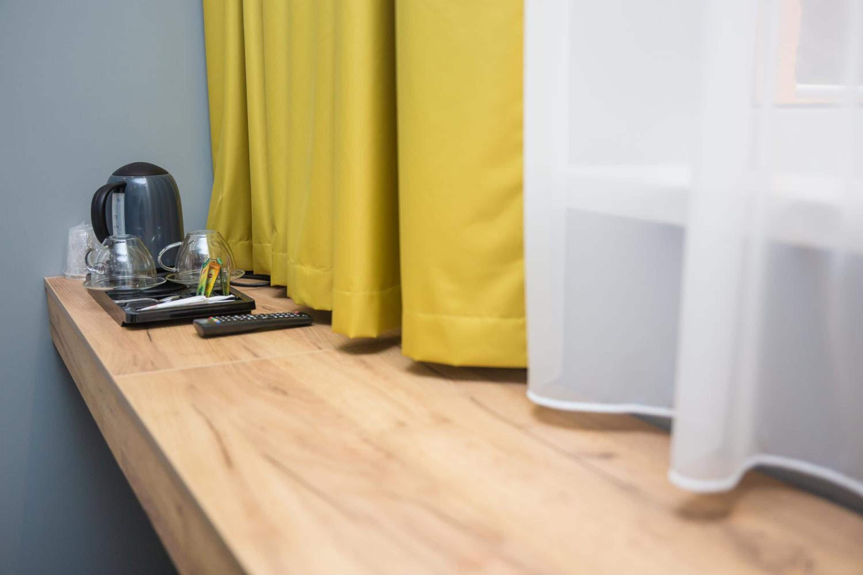 Una mesita de noche de madera con una tetera, una taza de vidrio, un control remoto y una caja de pañuelos.
