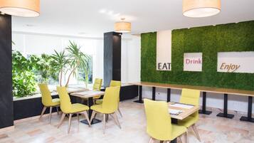 A modern dining area with yellow chairs, a long table, and a green wall with 'EAT', 'Drink', 'Enjoy' signs.